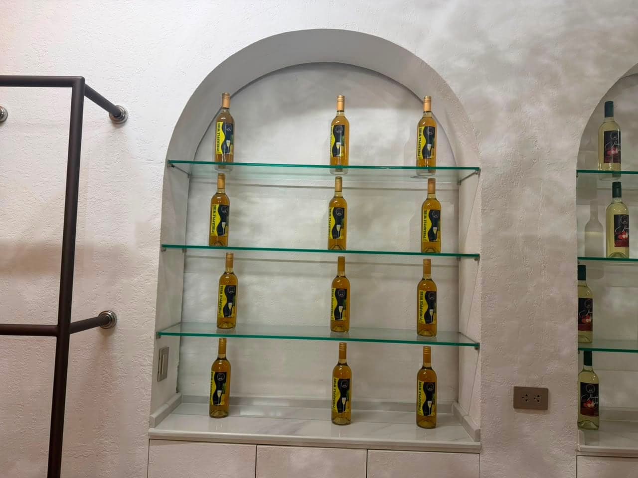 Bottles of ANA Pineapple Fruit Wine on glass shelves in an arched niche